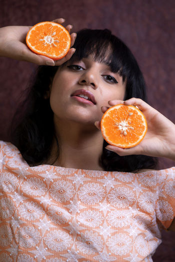 Close-up portrait of woman holding orange against wall