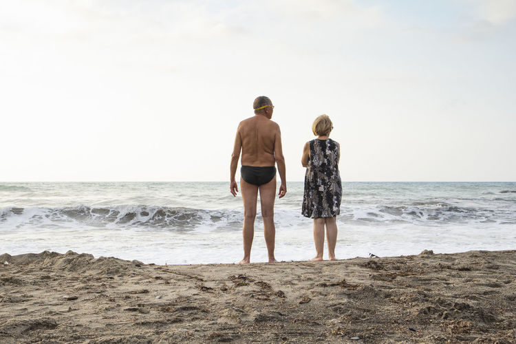 Italy, sicily, senior couple at the beach looking at the sea