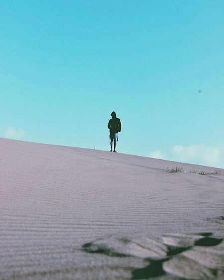 Man walking on sand dune against clear sky
