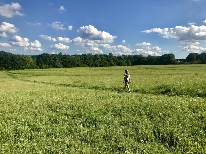 Young woman walking on grassy field against sky