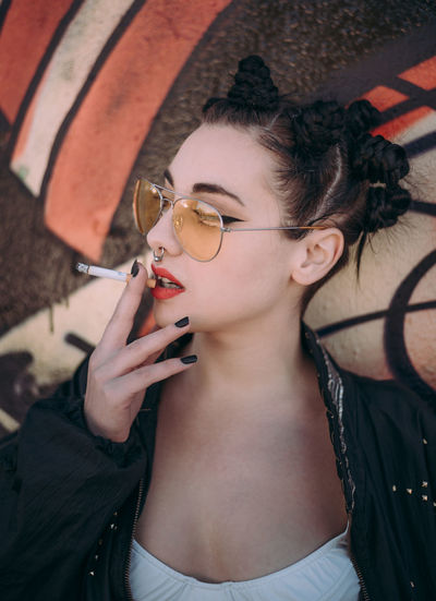 Close-up of young woman smoking cigarette by graffiti wall