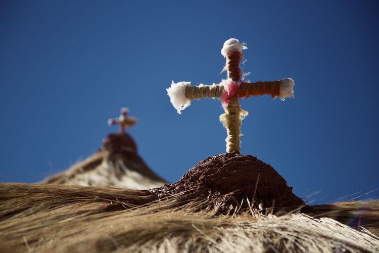 Low angle view of cross on land against clear blue sky