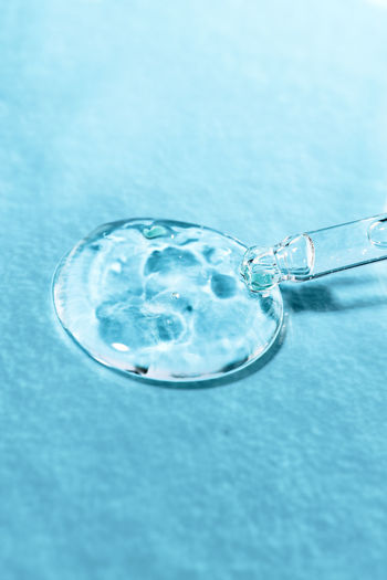 Cosmetic transparent gel close-up on a blue background with a glass pipette front view. a drop 