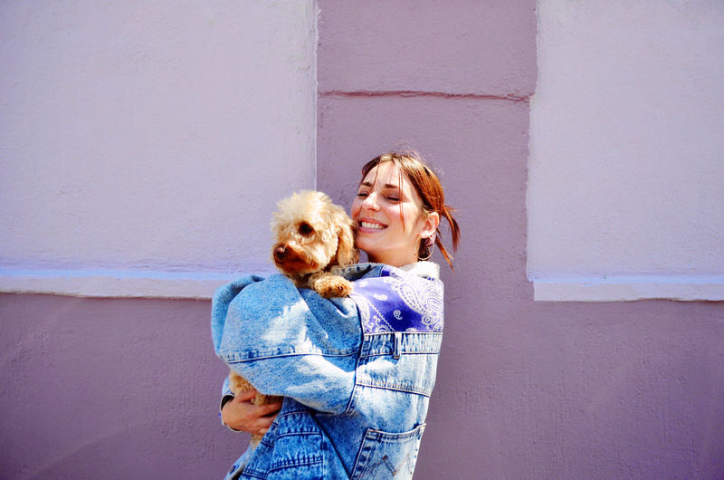 Happy woman with dog standing against wall