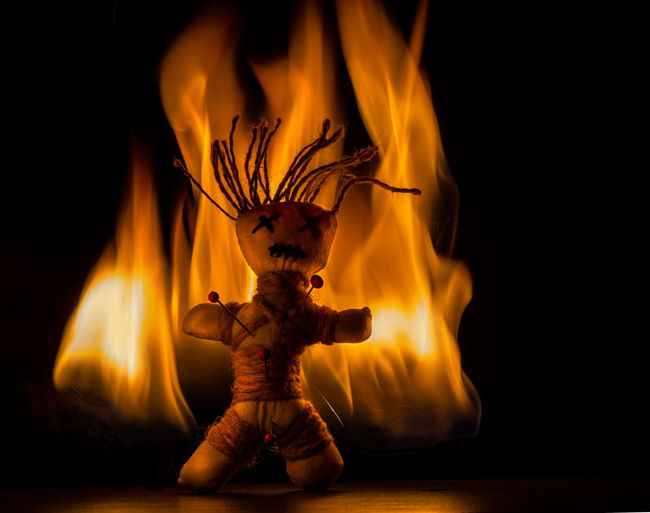 Close-up of voodoo doll and fire against black background