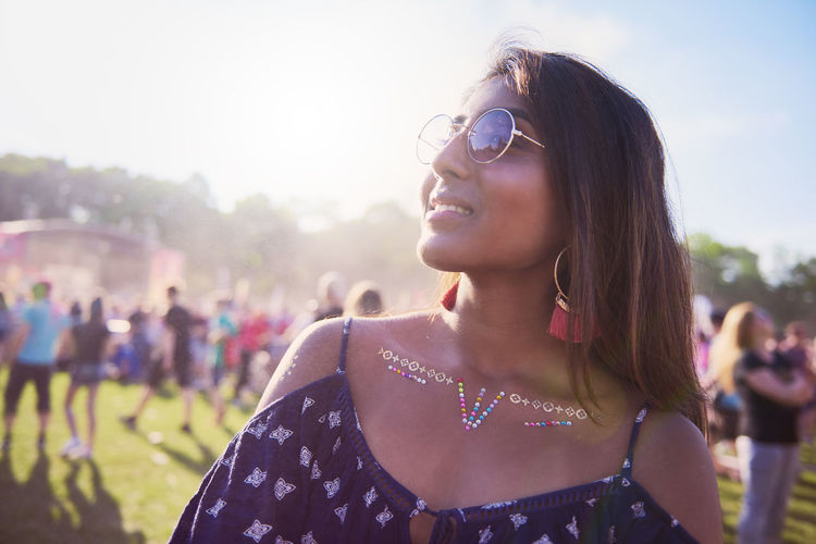 Smiling young woman wearing sunglasses while looking away in party during sunny day