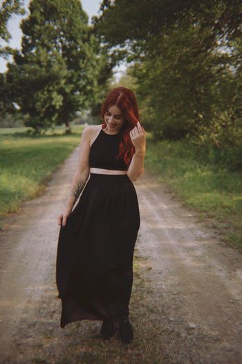 Full length of smiling young woman walking on dirt road against trees