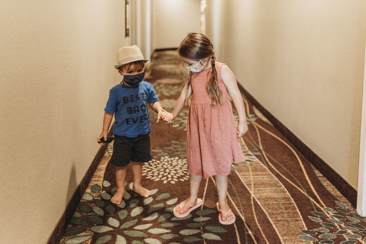 Young siblings wearing masks walking through hotel hallway together