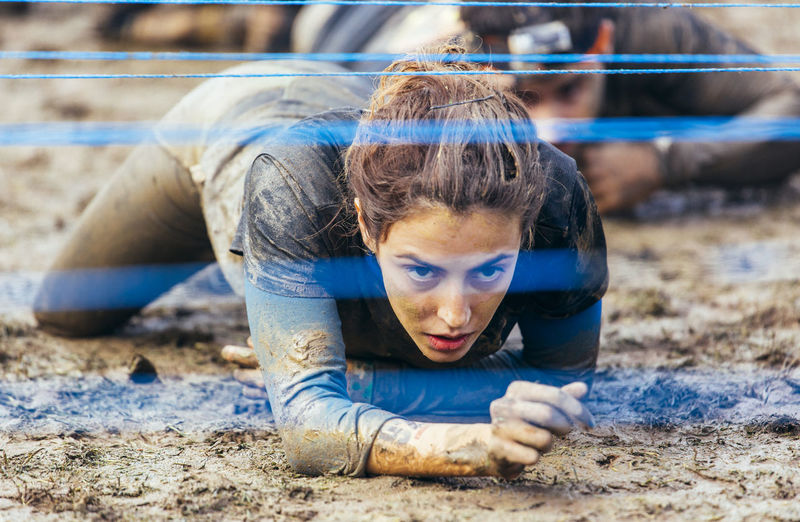 Participants in extreme obstacle race crawling under electric wire