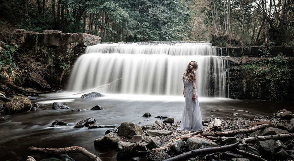 Woman standing by waterfall in forest