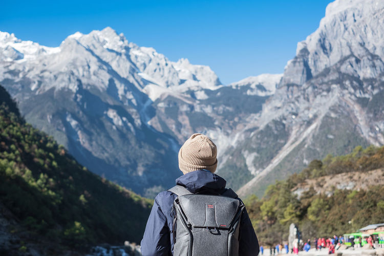 Rear view of man wearing backpack while standing against mountains during winter