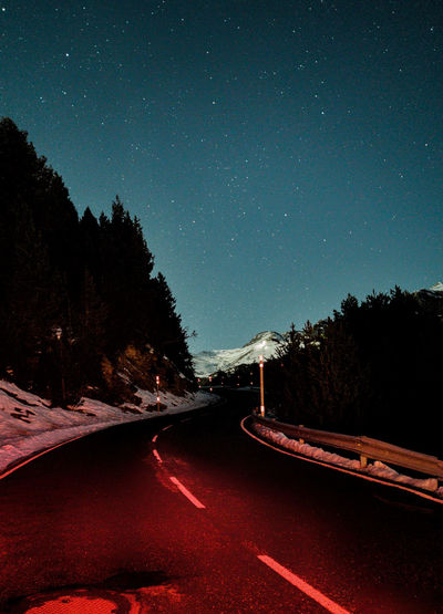 Road amidst illuminated trees against sky at night