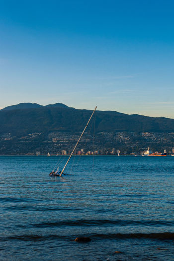 Sailboat drowning in sea against cityscape