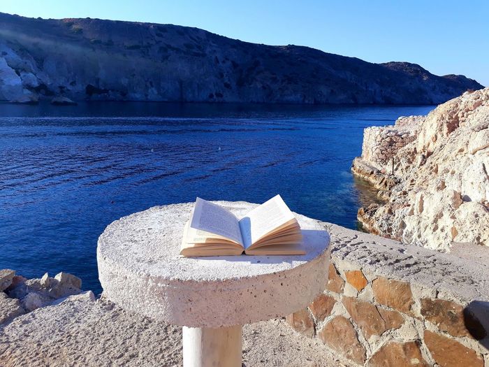 Book on a table on the seafront, milos, greece, september 2019