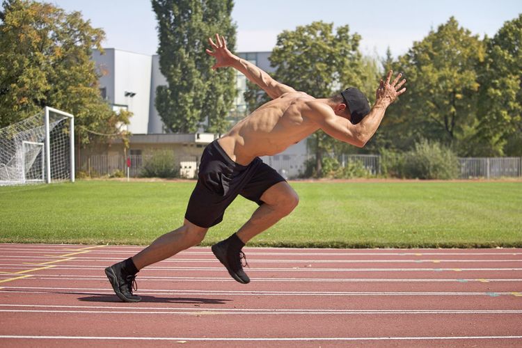 Side view of shirtless man running on track