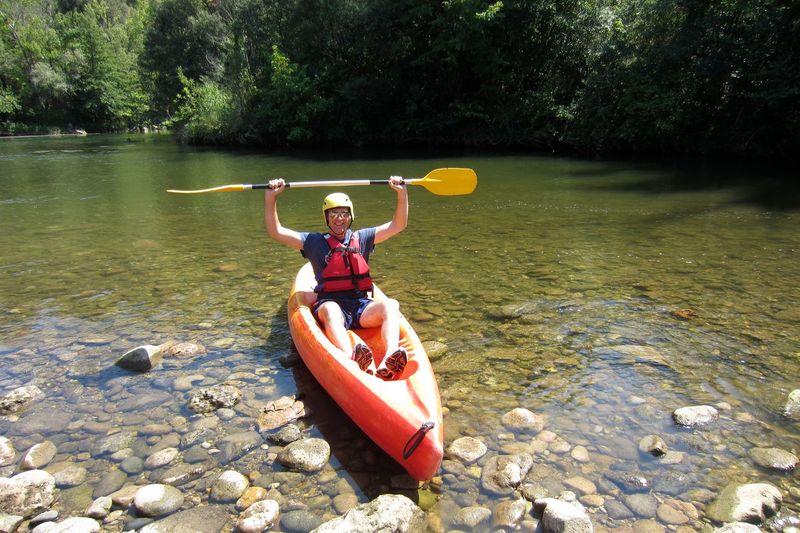 Excited man holding oar while sitting on kayak at riverbank