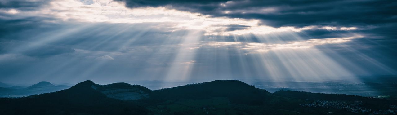 Sunlight streaming through clouds over silhouette mountains