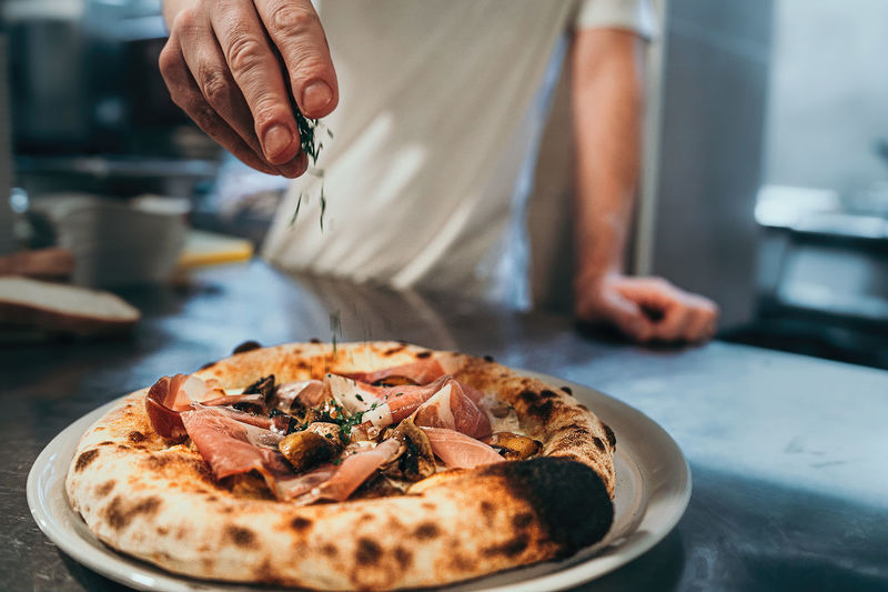An italian chef garnishes the pizza just out of the stone oven.