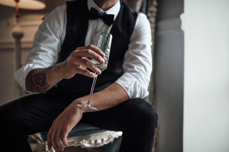 MIDSECTION OF MAN HOLDING DRINK SITTING IN GLASS