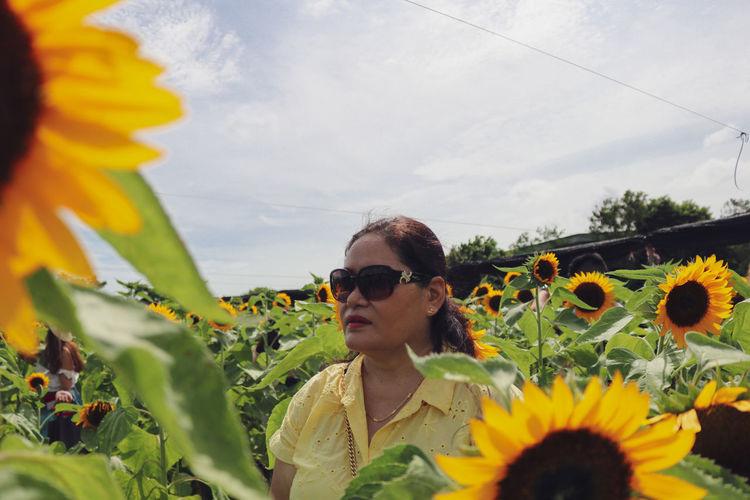 Portrait of young woman with sunflower amidst plants against sky