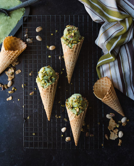Overhead view of pistachio ice cream in cones on black background.
