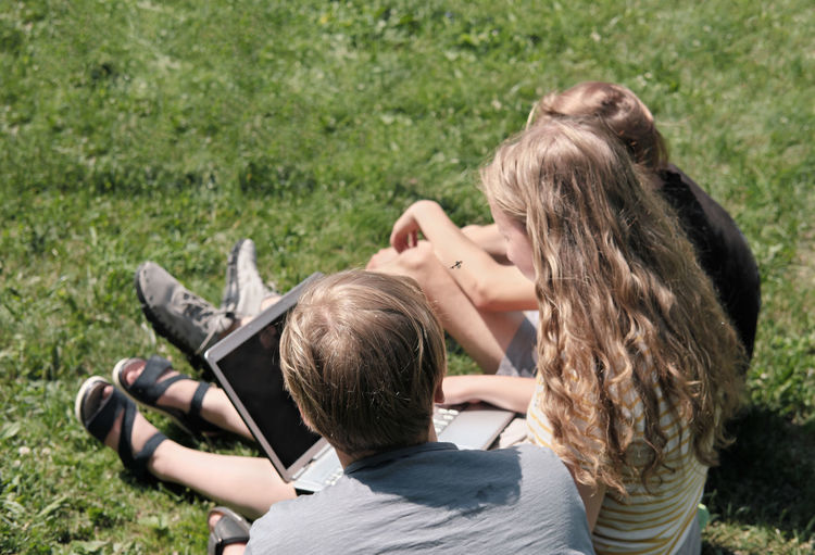 Group of teenagers using laptop for online chat outdoors. rear view of  boys and  girl with laptop