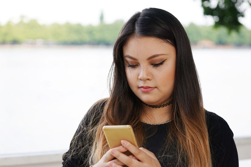 Young woman using mobile against lake