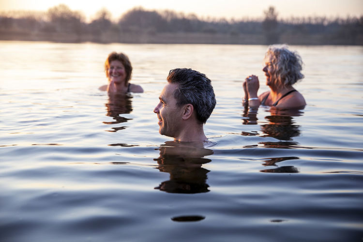 Smiling man looking away while female friends with hands clasped enjoying cold water during morning