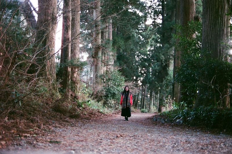 Full length of woman standing on road amidst trees in forest