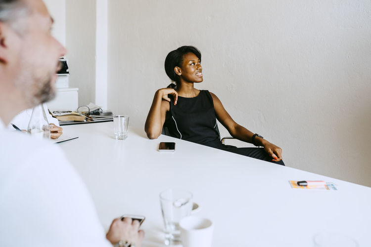Male and female colleagues looking away while sitting on conference table during seminar in office