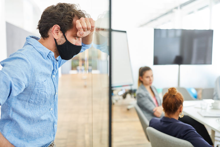 Businessman wearing mask standing against colleagues in office