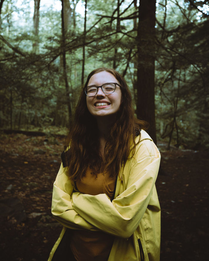 PORTRAIT OF SMILING WOMAN STANDING IN FOREST