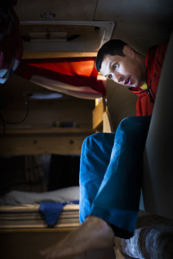 Man waking up from bunk bed inside converted school bus dressed up