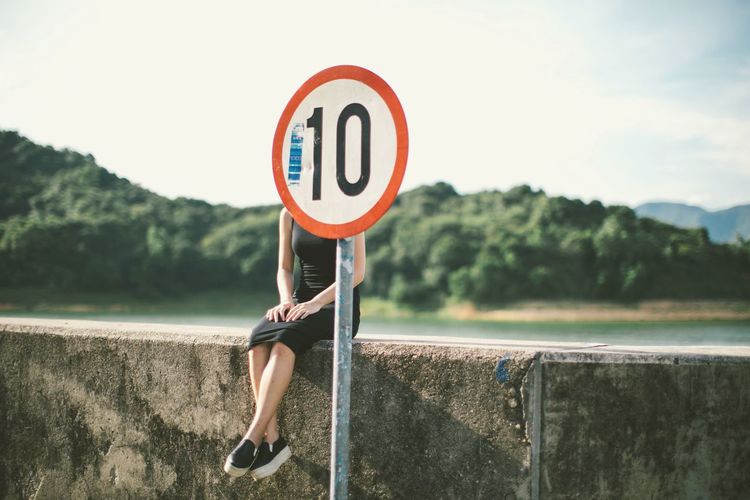 Woman sitting on retaining wall behind speed limit signboard
