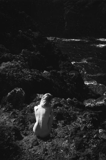Rear view of naked woman sitting on rock at beach