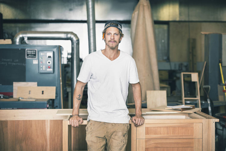 Portrait of confident carpenter leaning on cabinet in workshop