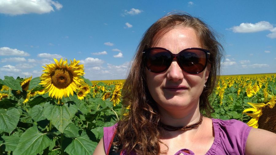 Close-up portrait of woman wearing sunglasses while standing at sunflower farm