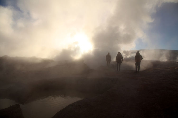 Tourists watching steam rising from geyser at salar de uyuni
