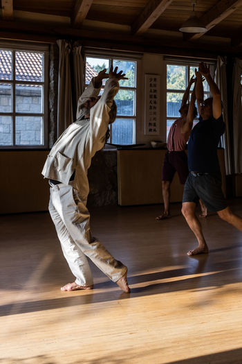 Full body side view of unrecognizable male instructor doing chi kung or qigong movement with arms raised during practice with students