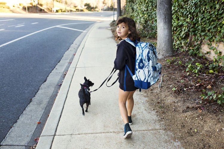 Rear view portrait of girl walking with dog on sidewalk