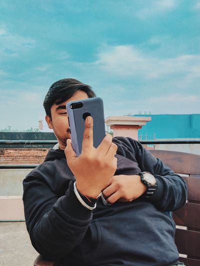 Portrait of young man using mobile phone against sky