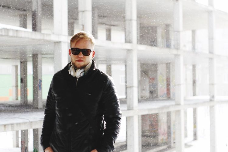 Portrait of young man wearing sunglasses standing against building during snowfall