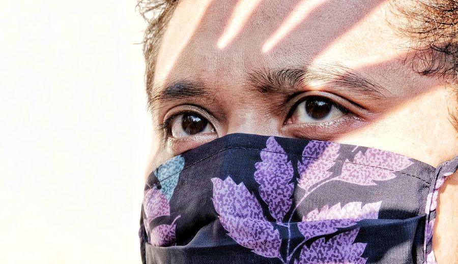 Close-up portrait of man covering face with face mask against white background