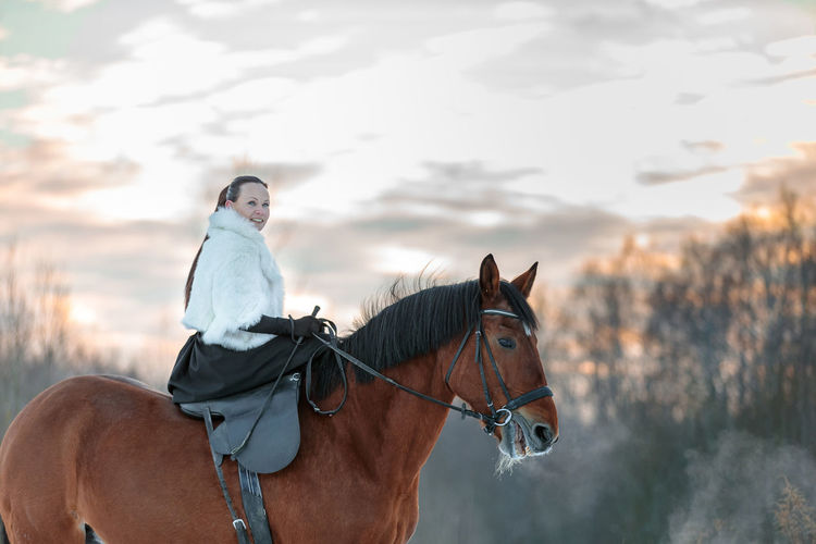 Side view of woman riding horse against sky