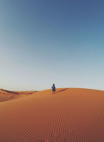 Man walking in desert against clear blue sky
