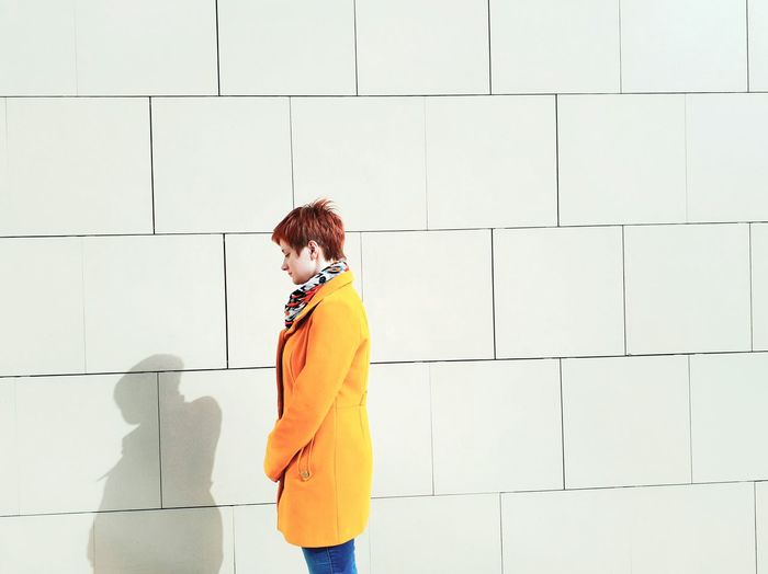 Side view of woman wearing yellow winter coat standing against white wall