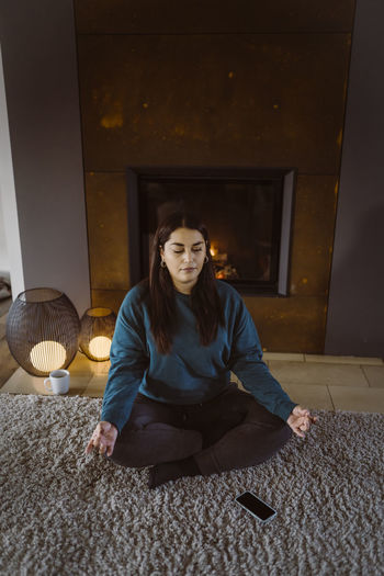 Woman practicing yoga while sitting cross-legged on carpet at home