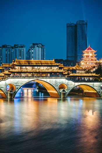 Arch bridge over river in city at night