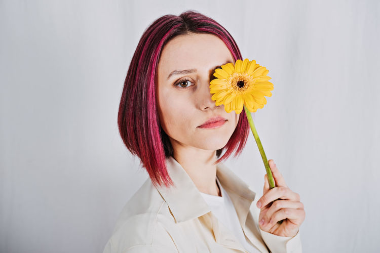 Studio portrait millennial woman with bright red color hair and yellow flower.