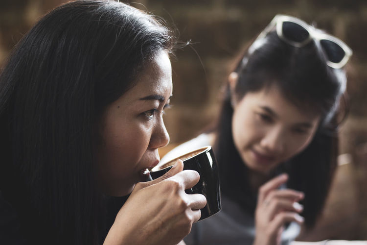 Woman drinking coffee while friend talking in background
